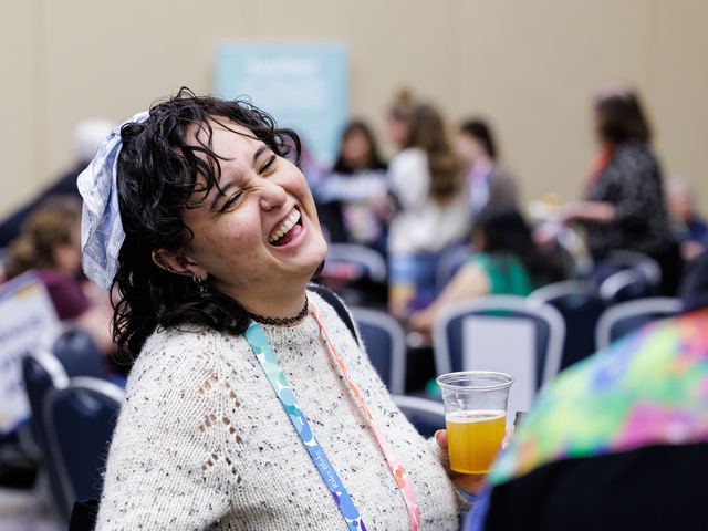An attendee laughing with a drink in hand at the h+h americas happy hour