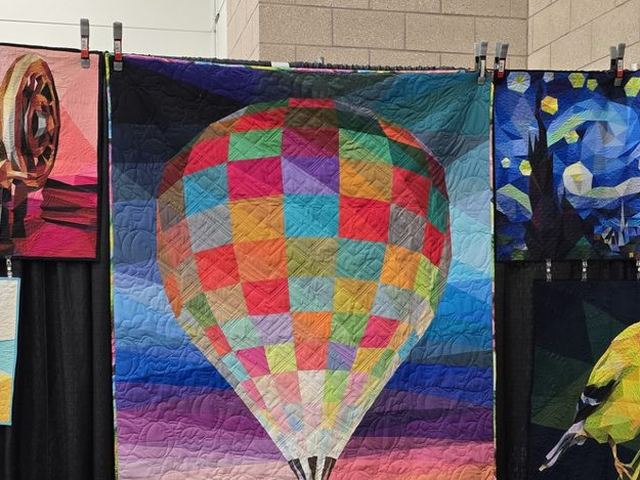 A foundation paper-pieced hot air balloon quilt hanging in a display