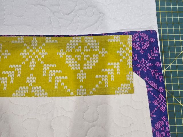 The corner of a Loter&iacute;a quilt, with a yellow patterned strip and purple binding