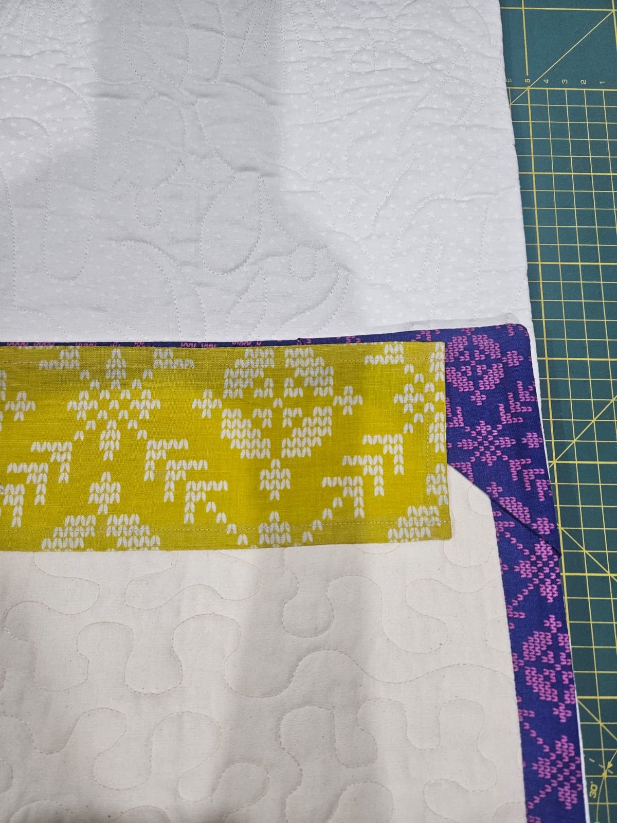 The bound corner of a Loter&iacute;a quilt, where the yellow patterned strip meets the purple and pink binding